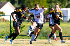 A female soccer player splits two defenders as she kicks the ball.